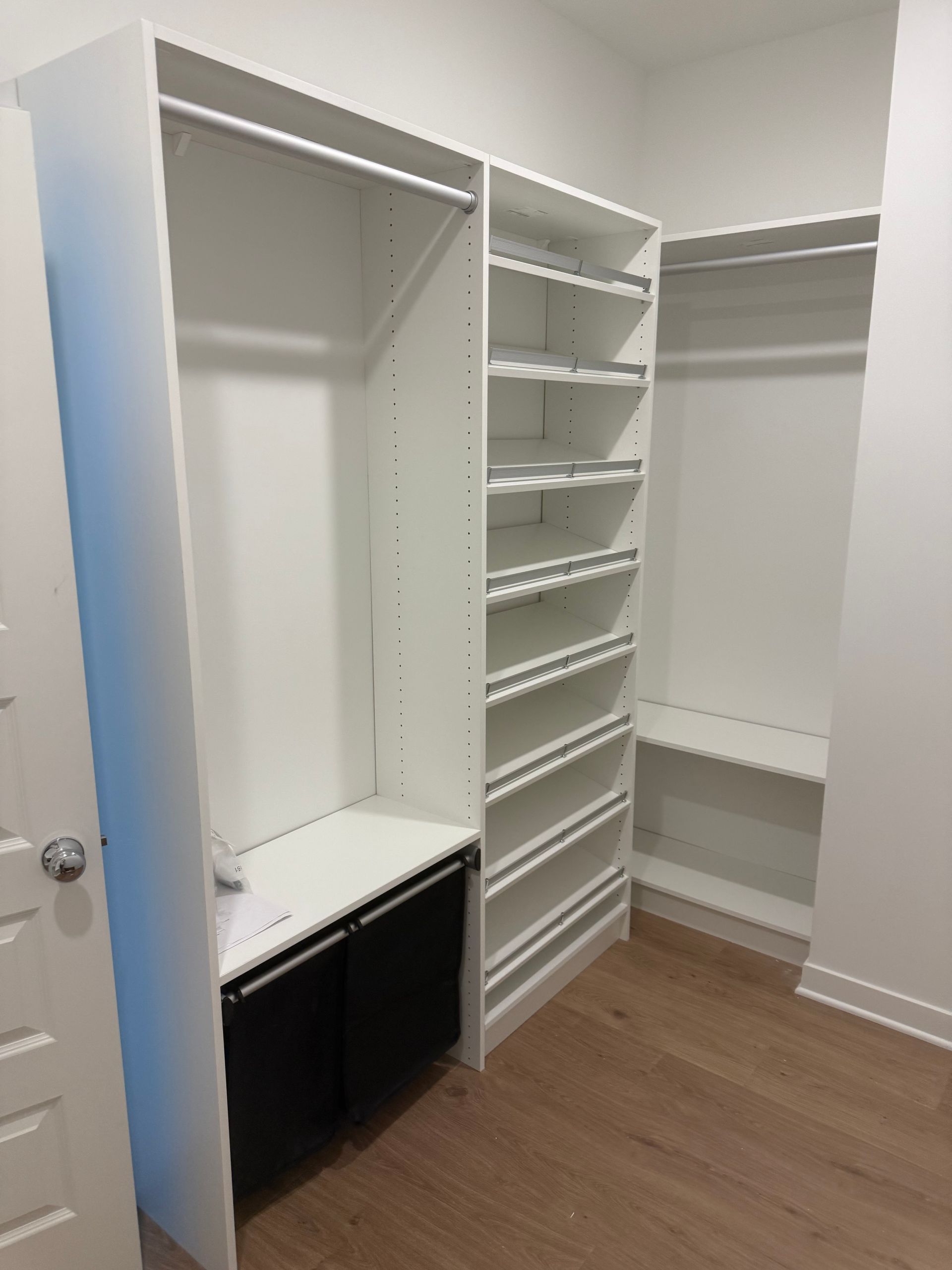 Open walk-in closet with white shelving, hanging rods, and a built-in desk above a black cabinet.