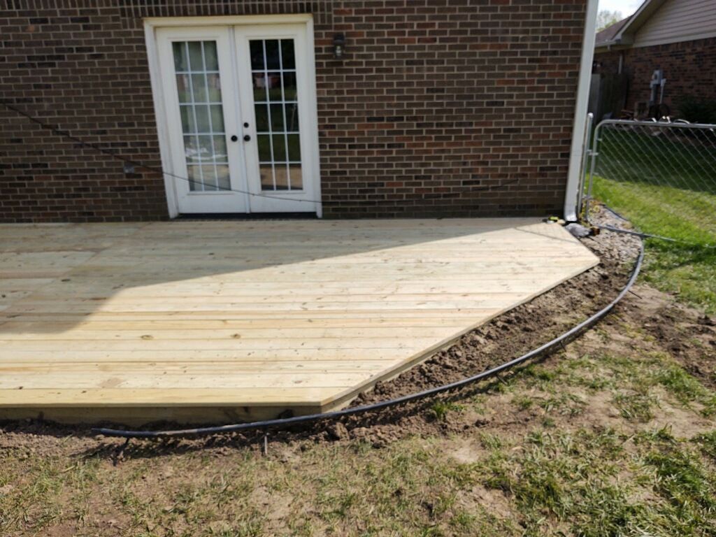 Wooden patio deck beside a brick house with white French doors, curving along the yard edge
