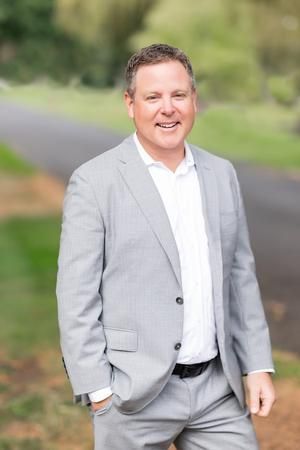A man in a suit and white shirt is standing with his hands in his pockets.