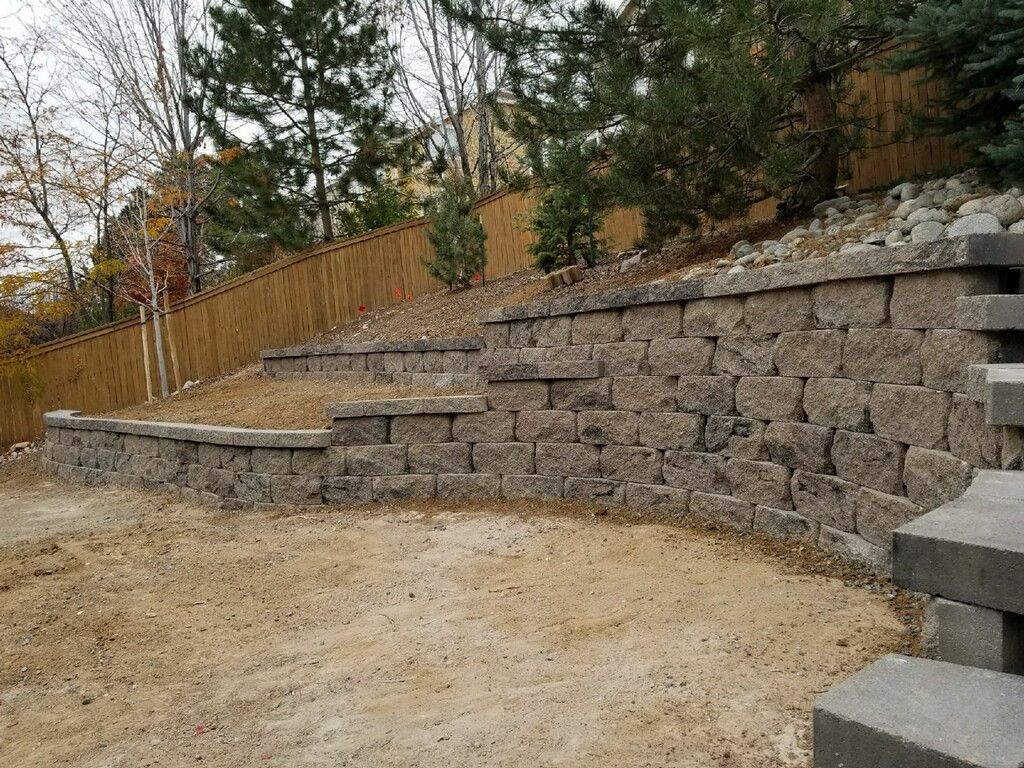 A stone wall is sitting on top of a dirt hill next to a wooden fence.