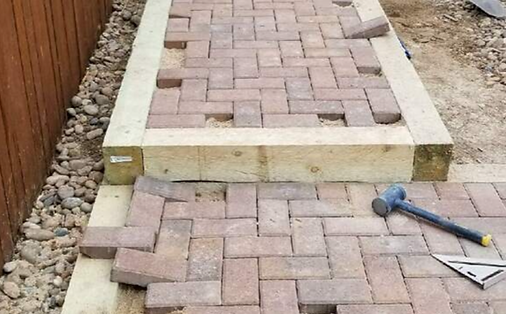 A brick walkway is being built next to a wooden fence.