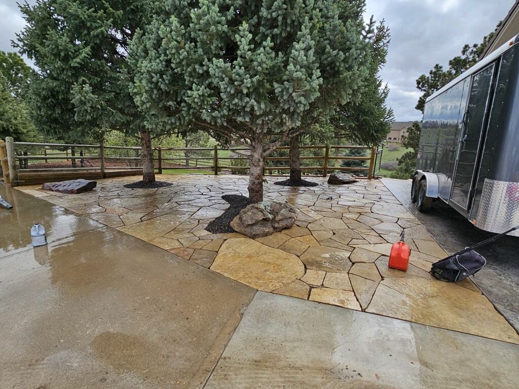 A trailer is parked in a driveway next to a tree.