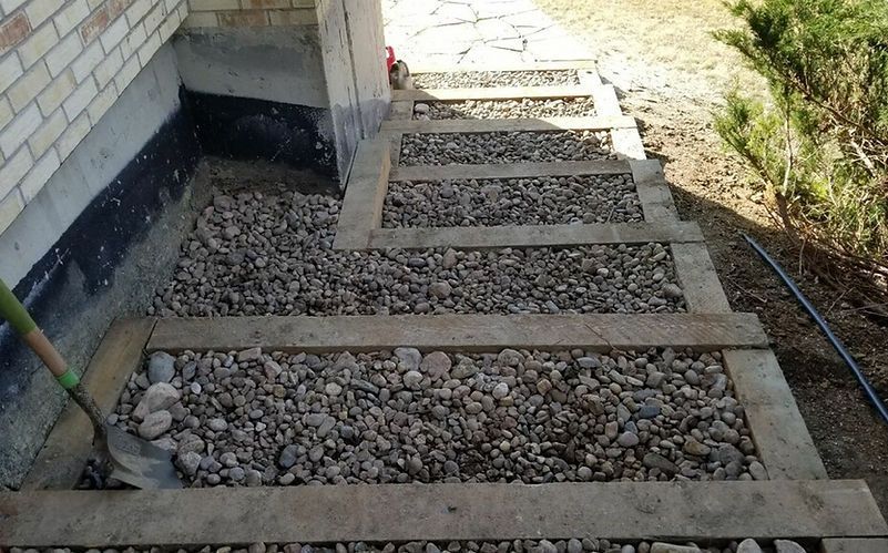 A shovel is sitting on a gravel path next to a brick building.