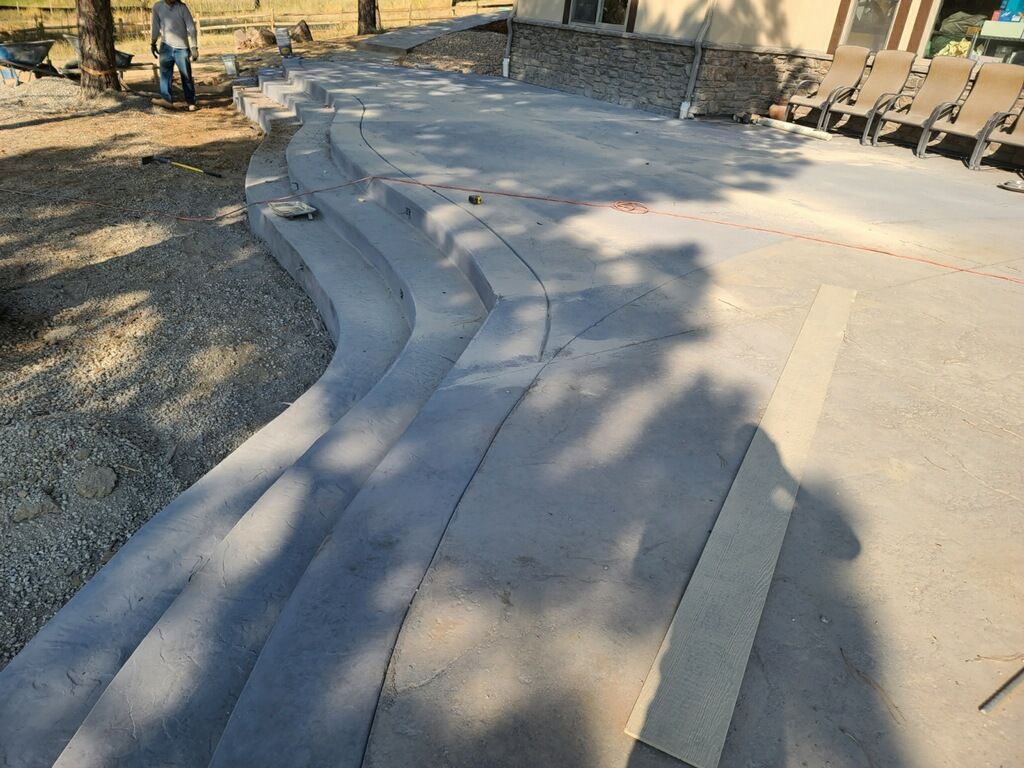 Concrete patio with curved steps under construction; worker standing nearby.