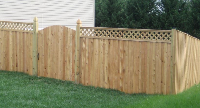 Wooden fence with lattice top, surrounding a grassy yard near a building and trees.