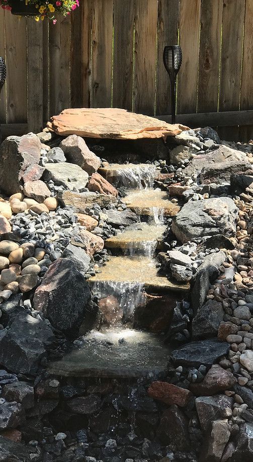 A Small Waterfall is Surrounded by Rocks and a Wooden Fence