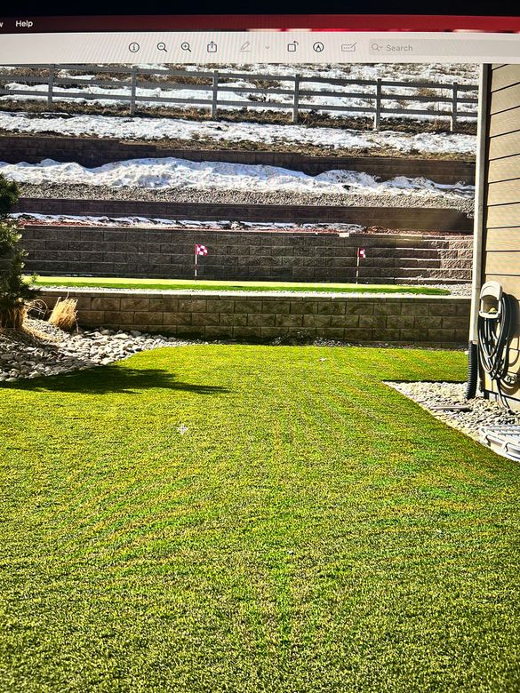 Green lawn with mini golf course, brown retaining walls, snowy hillside, and a wooden fence.