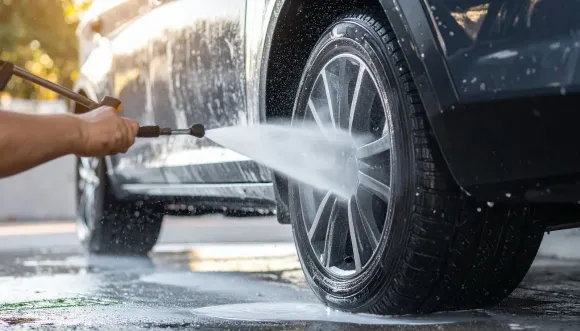 Person washing a black car tire with a pressure washer, surrounded by soapy water.