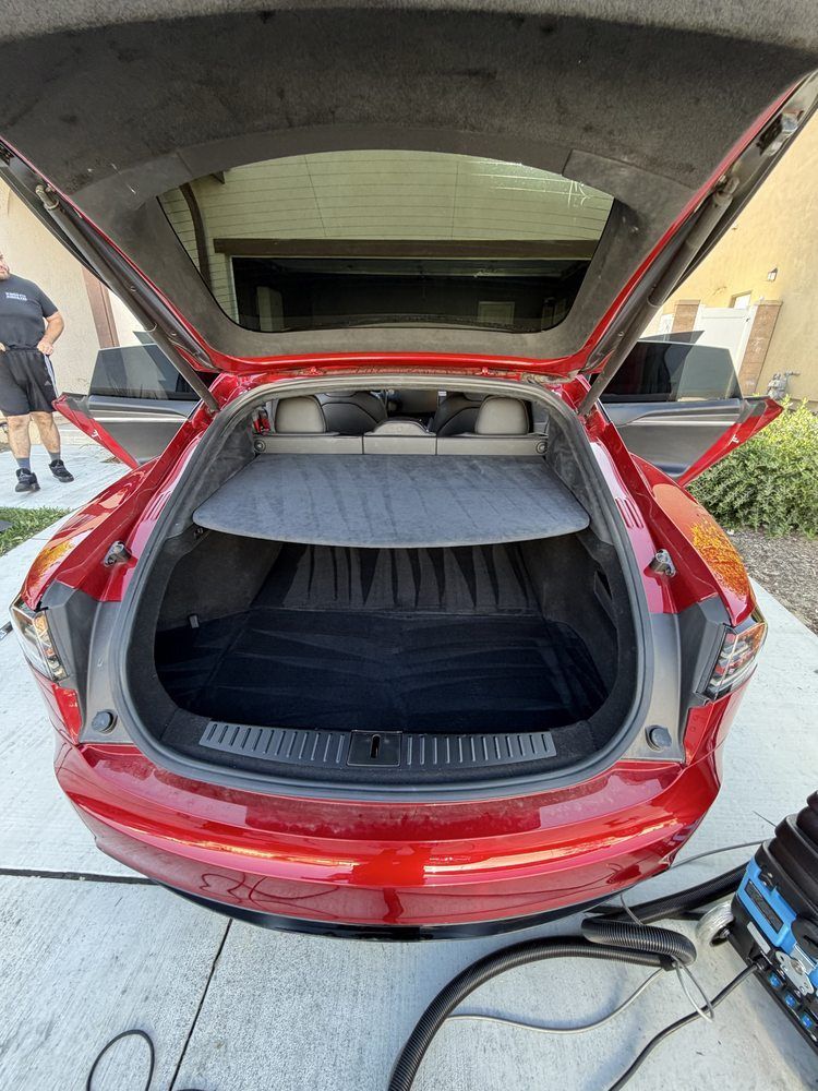 Red hatchback car with open trunk. A person stands nearby.