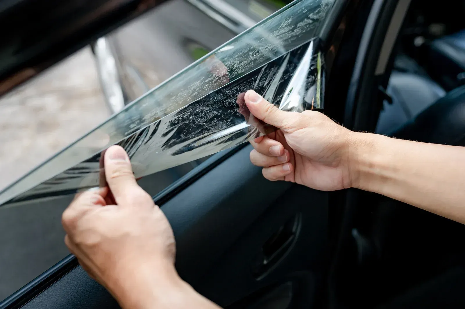 Hands peeling protective film from a car window.
