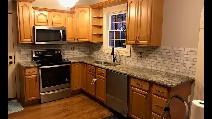 Modern kitchen with white cabinets, marble counters, and overhead lighting.