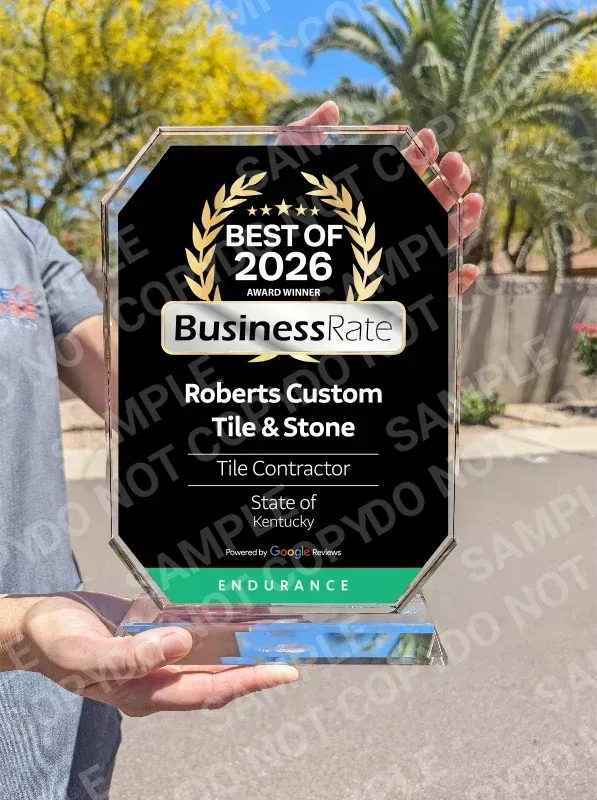 A person holds a black, hexagonal plaque for Roberts Custom Tile & Stone, the