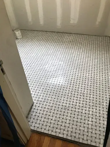 A gloved hand uses a mallet to tap a tile into place on a patterned floor.