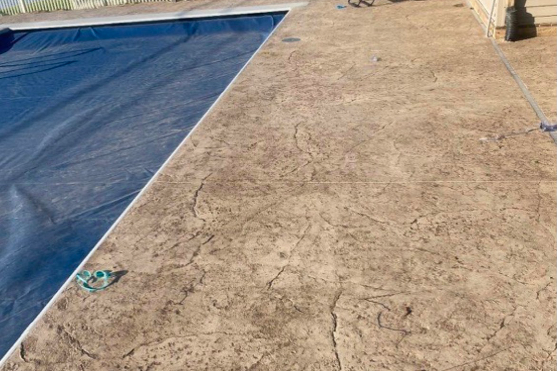 A concrete patio next to a swimming pool with a blue cover on it