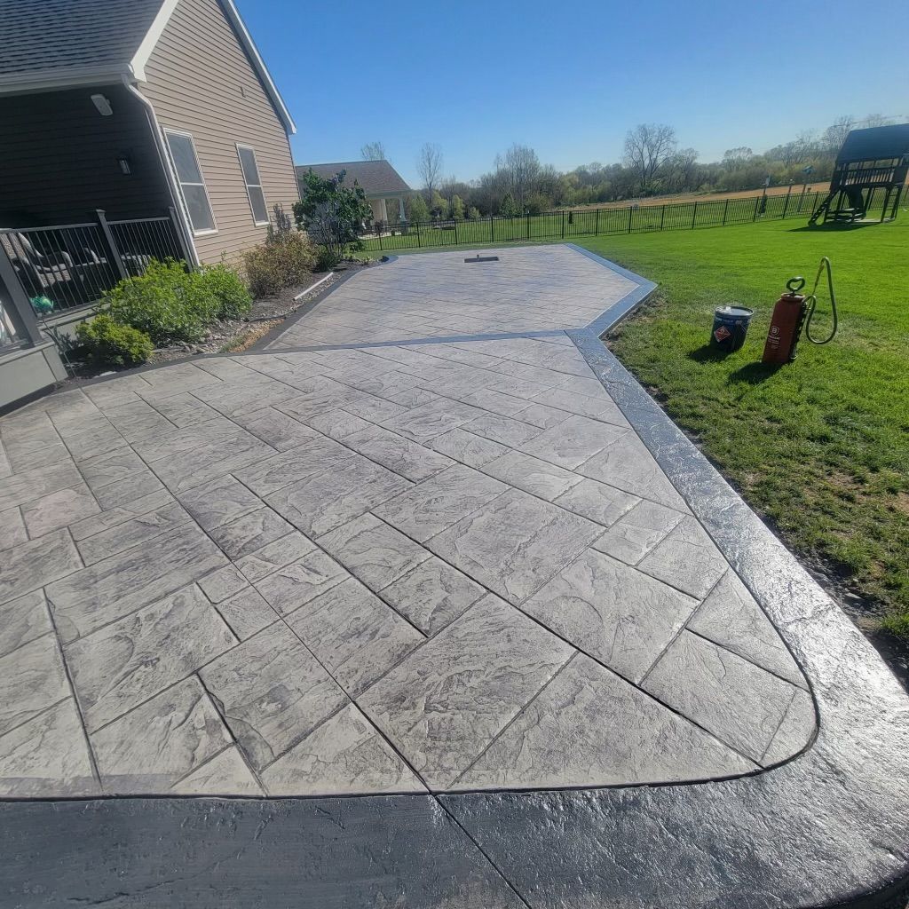 Stamped concrete patio in a backyard setting with a house visible.