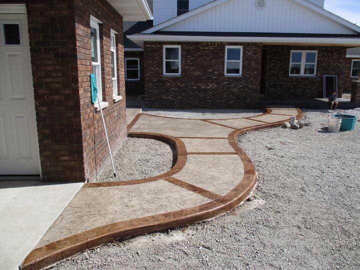 Concrete walkway with decorative brown border leading to brick buildings.