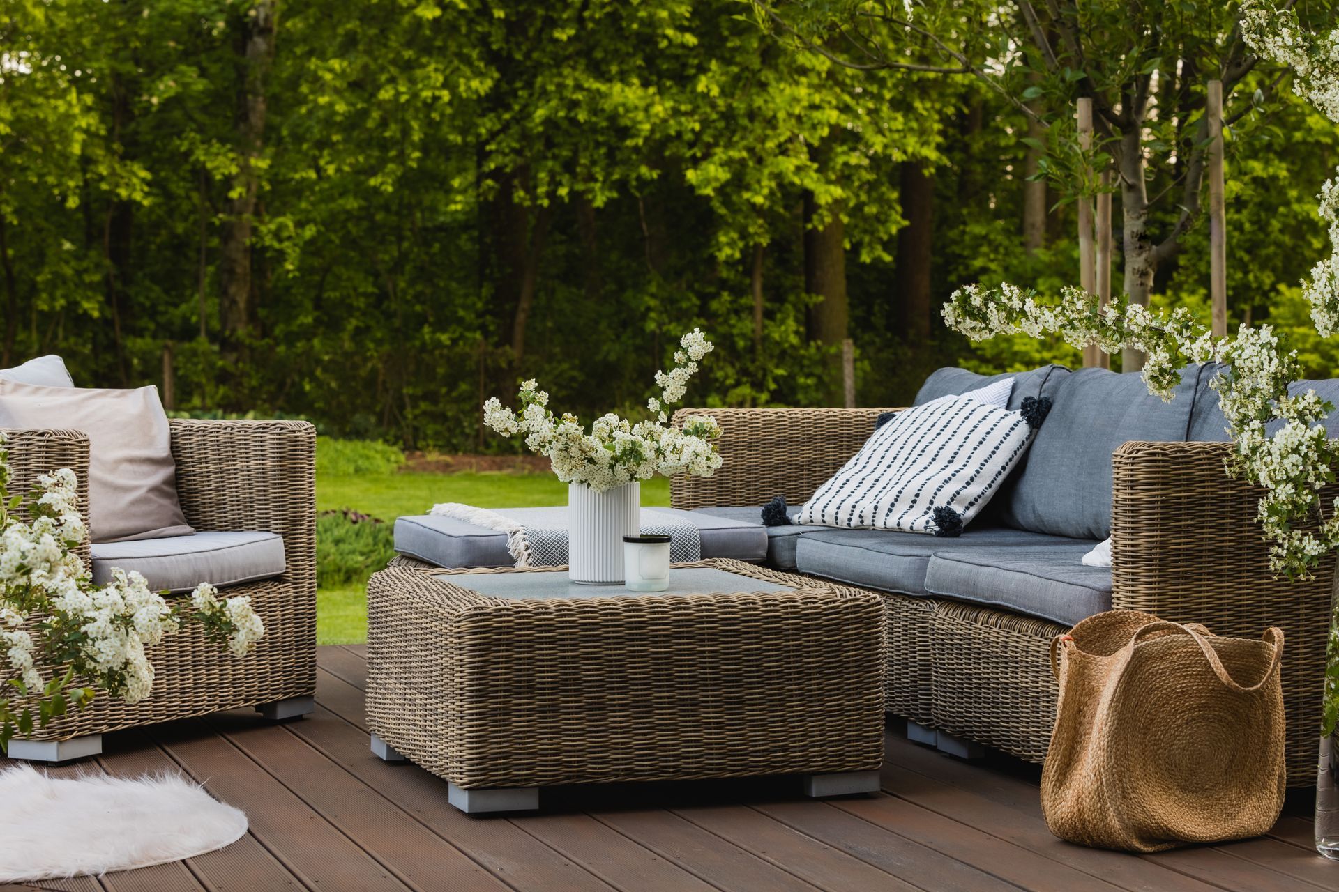 Outdoor wicker patio seating with blue cushions, coffee table, and flowers on a deck surrounded by greenery