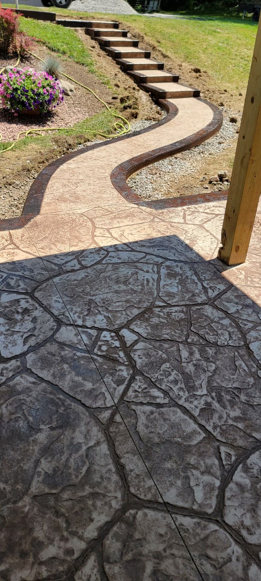Concrete pathway with steps and a patio with a stone-like texture. Green grass and landscaping visible.