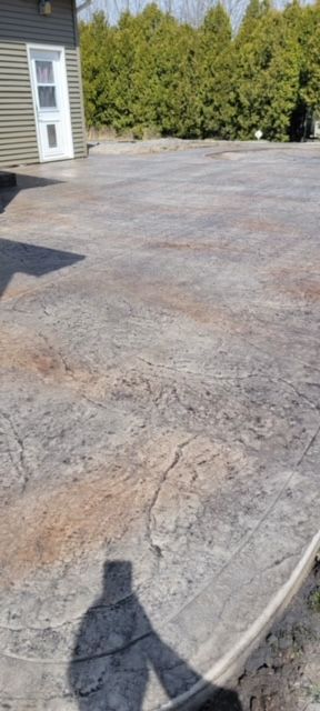 Stamped concrete patio with a building on the left and trees in the background. A shadow is cast on the concrete.