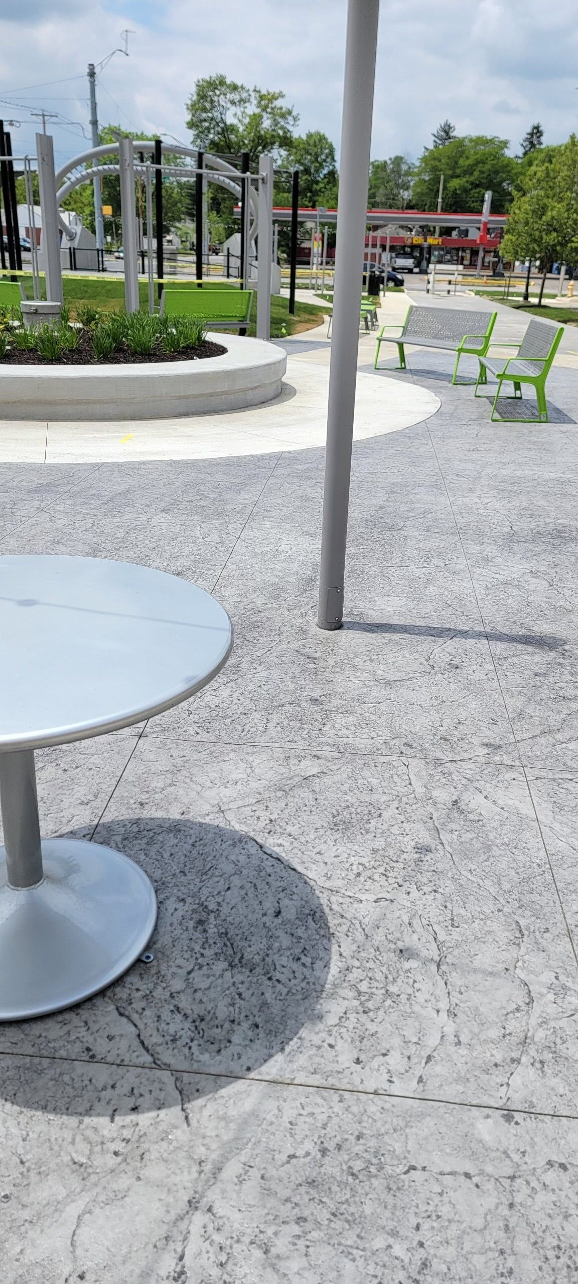 A public park scene with a silver table, gray gravel, and green chairs.