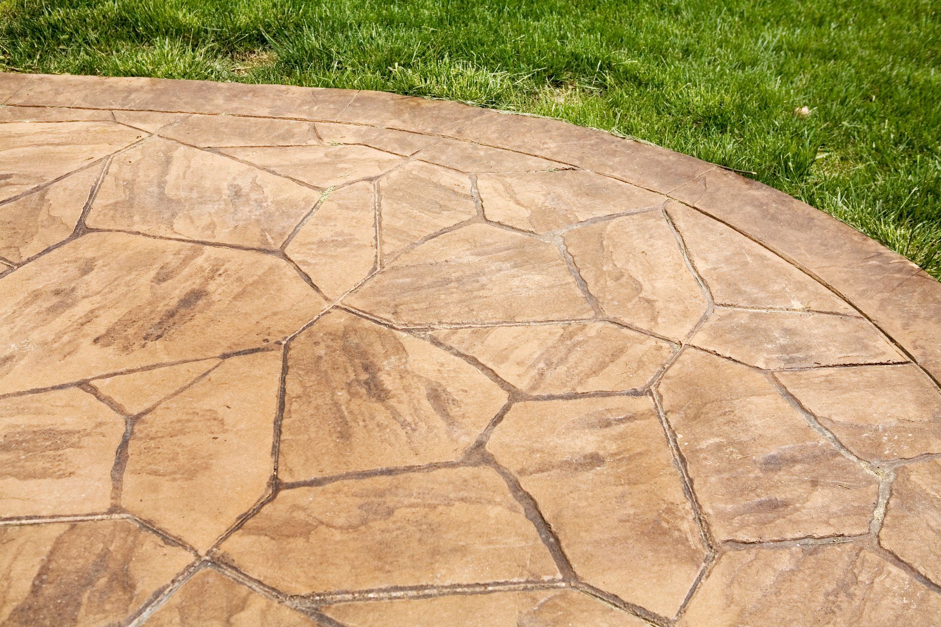 Stamped concrete patio with a stone-like pattern bordered by green grass in a backyard.