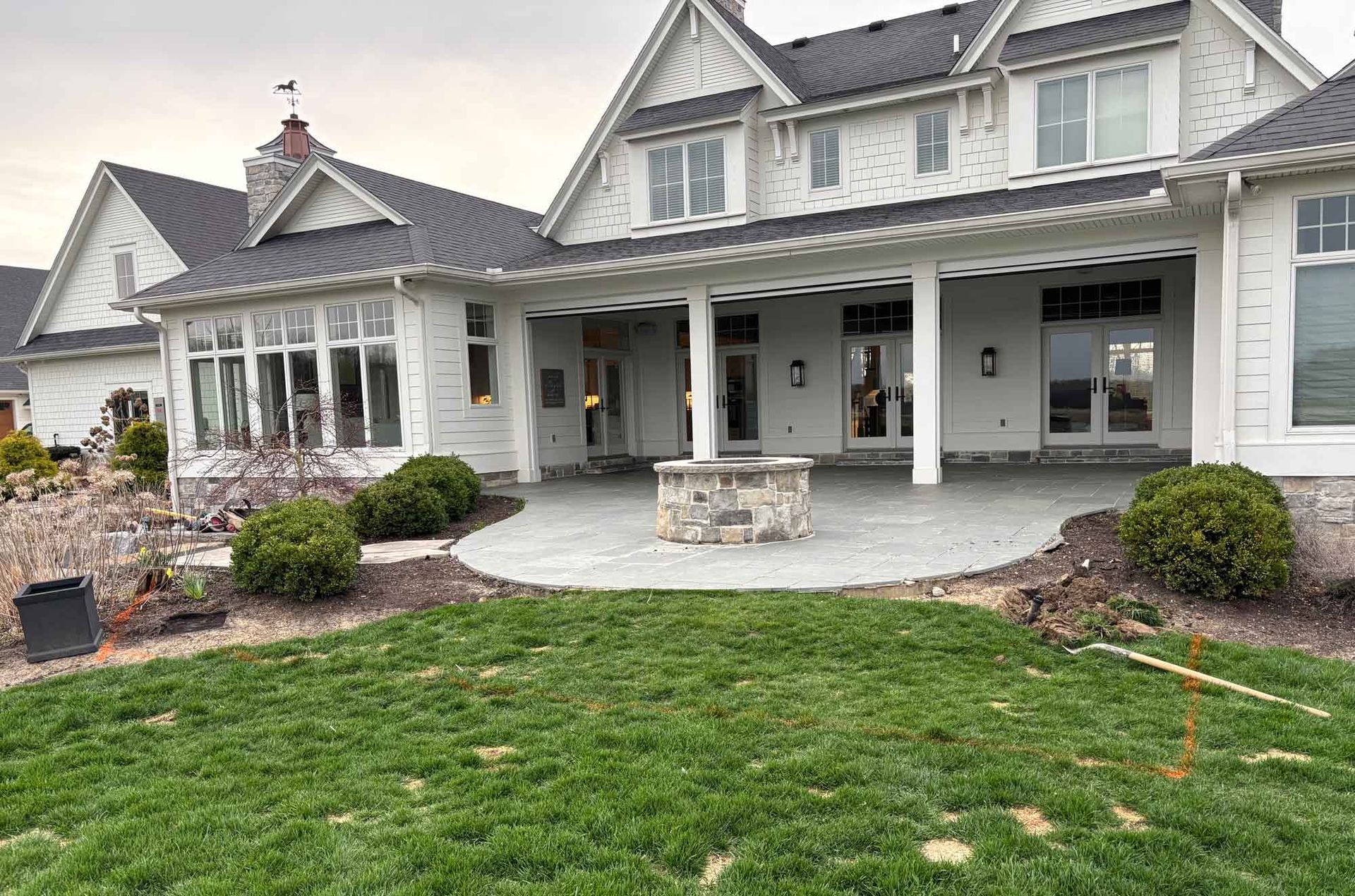 Large gray-and-white house with a covered porch, stone patio, and green front lawn