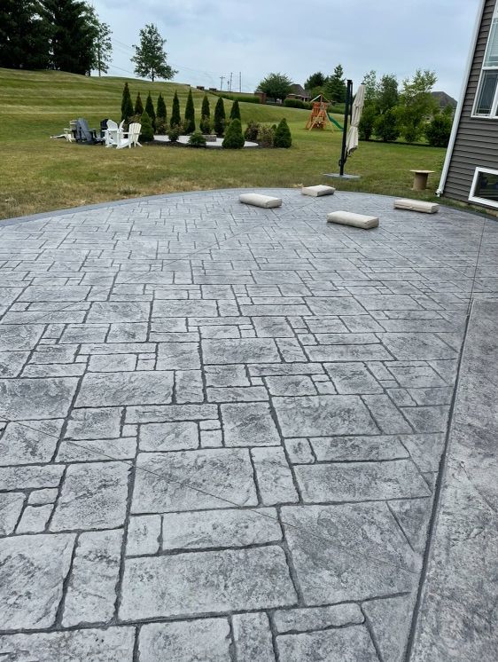 Gray stamped concrete patio with decorative stone layout, green lawn background.