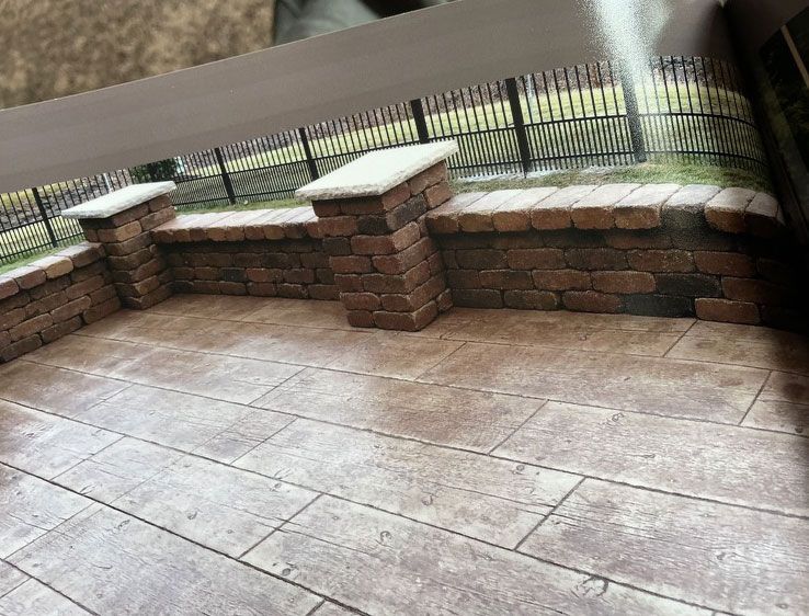 Brick patio with low wall, pillars, and a black metal fence in the background.