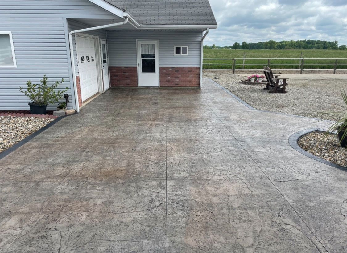Concrete driveway leading to a garage and small building, with a field in the background.