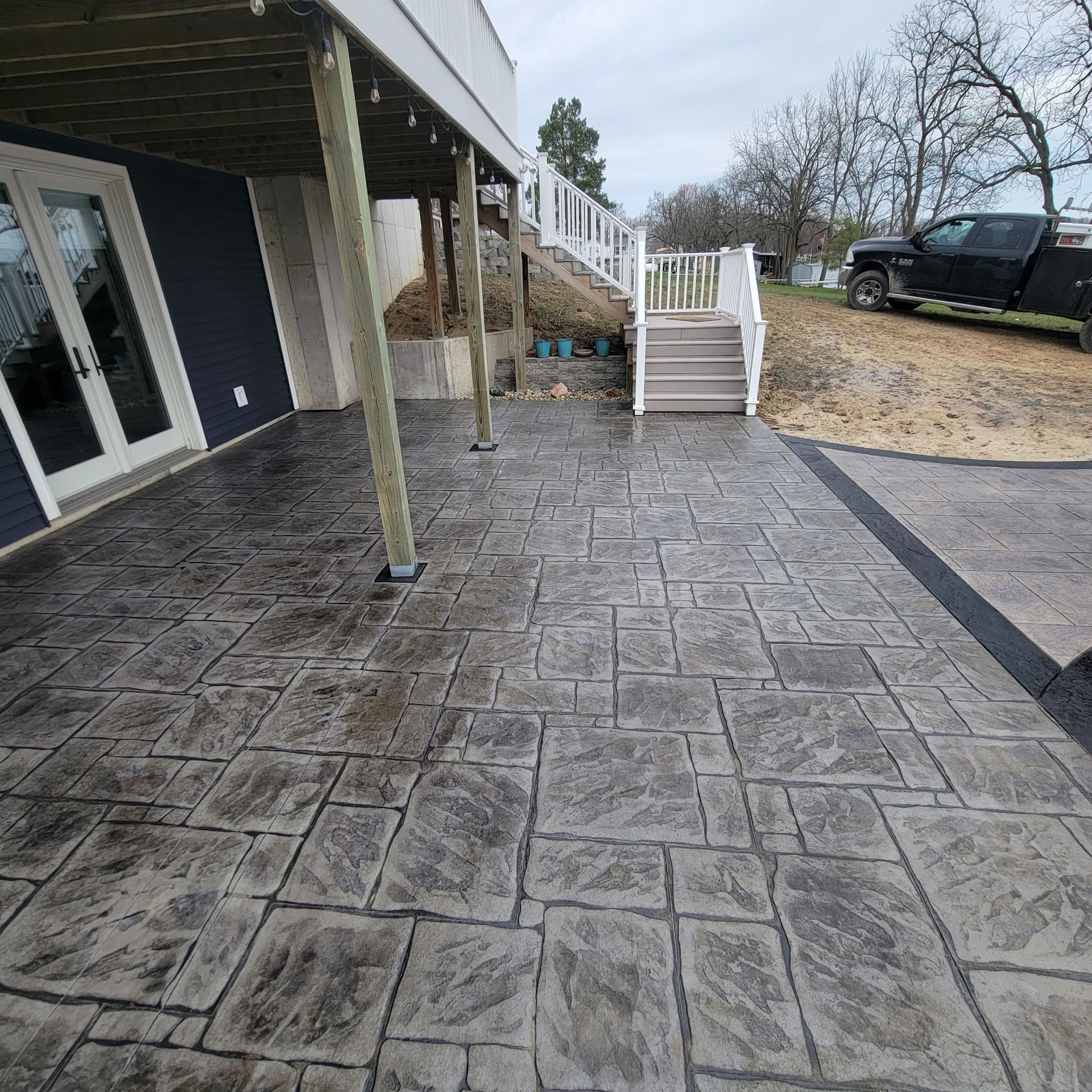 Stamped concrete patio with steps leading up to a deck, near a house and a parked truck.