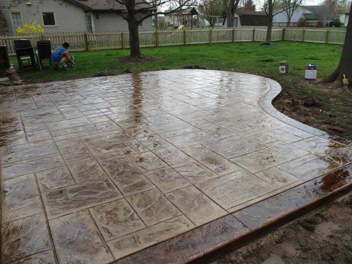 Wet stamped-concrete patio in a backyard, with a curved edge and houses in the background