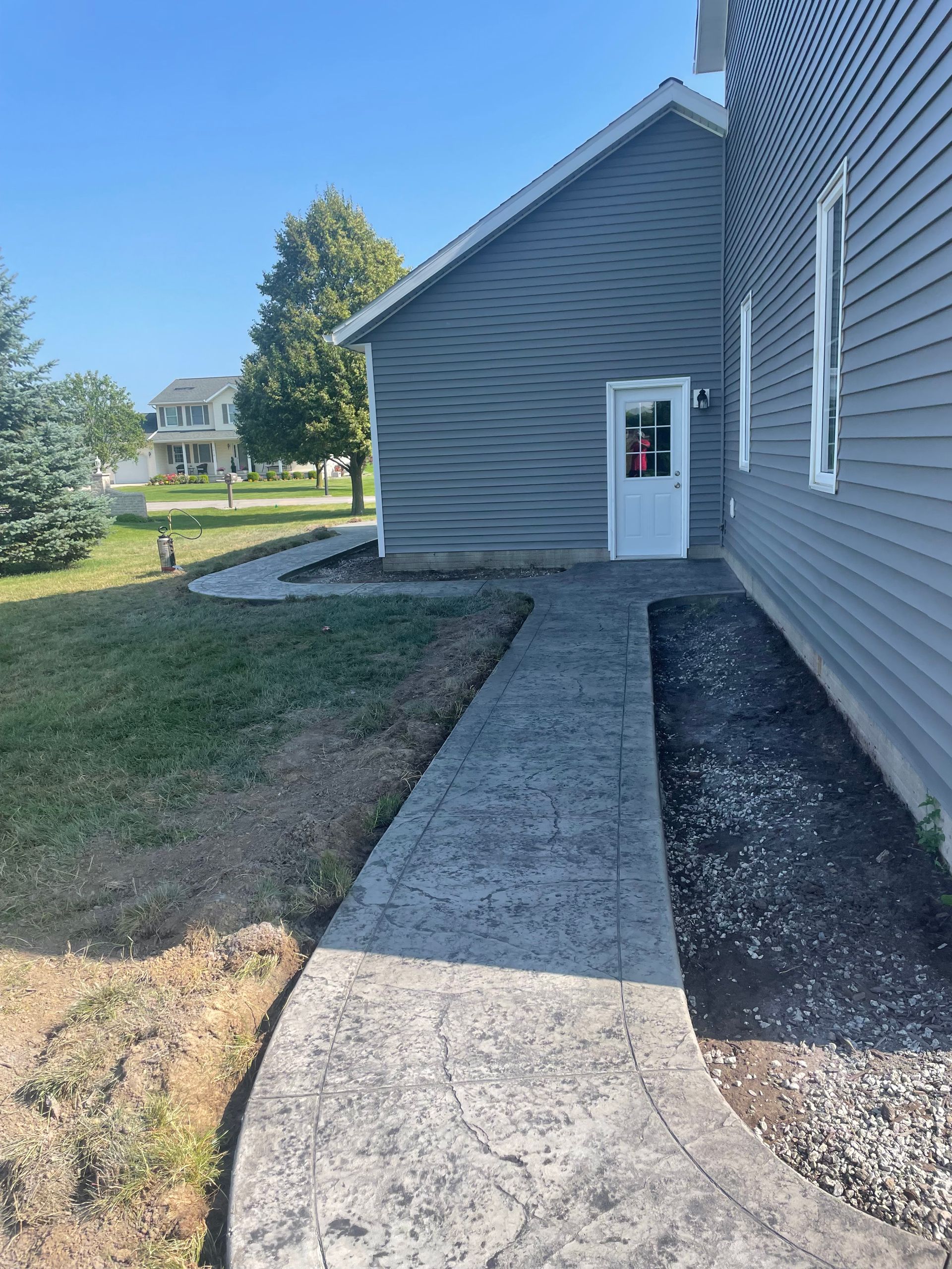 Concrete walkway beside gray house leads to white side door. Concrete walkway beside gray house leads to white side door.