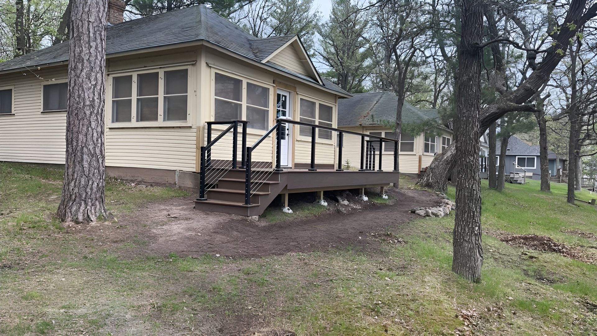 Wooden cabin with a front porch and steps, set among trees on a grassy slope