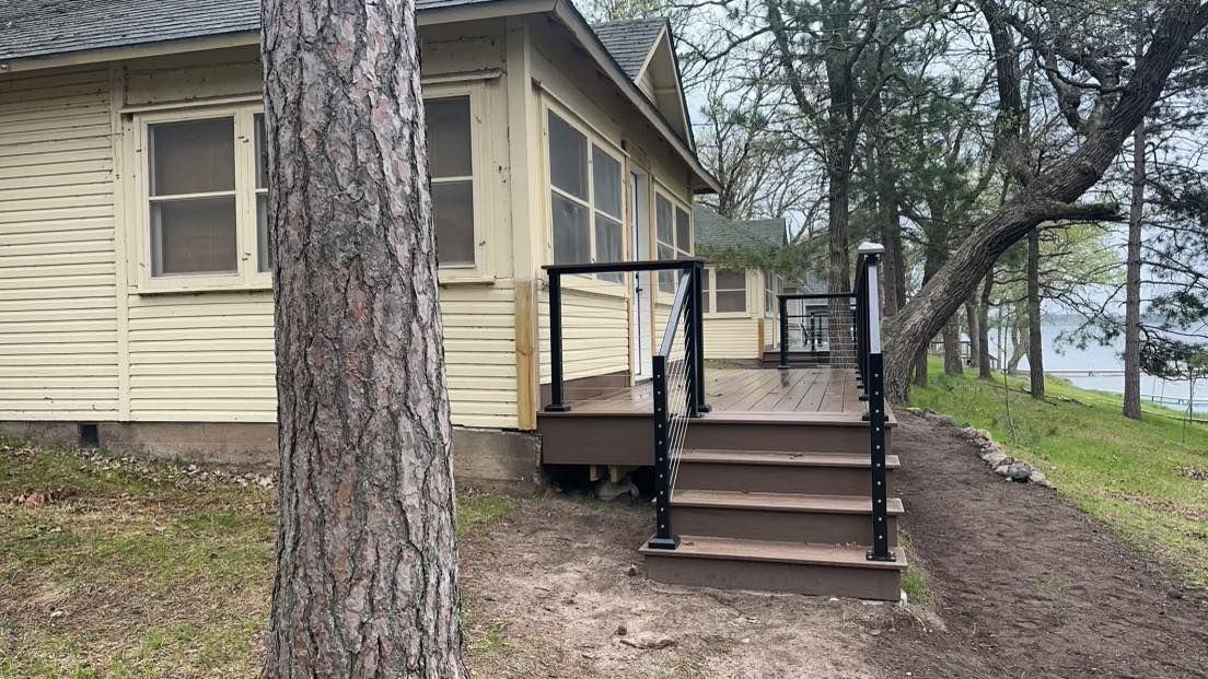House with front steps and railing beside a large tree near a lakeshore