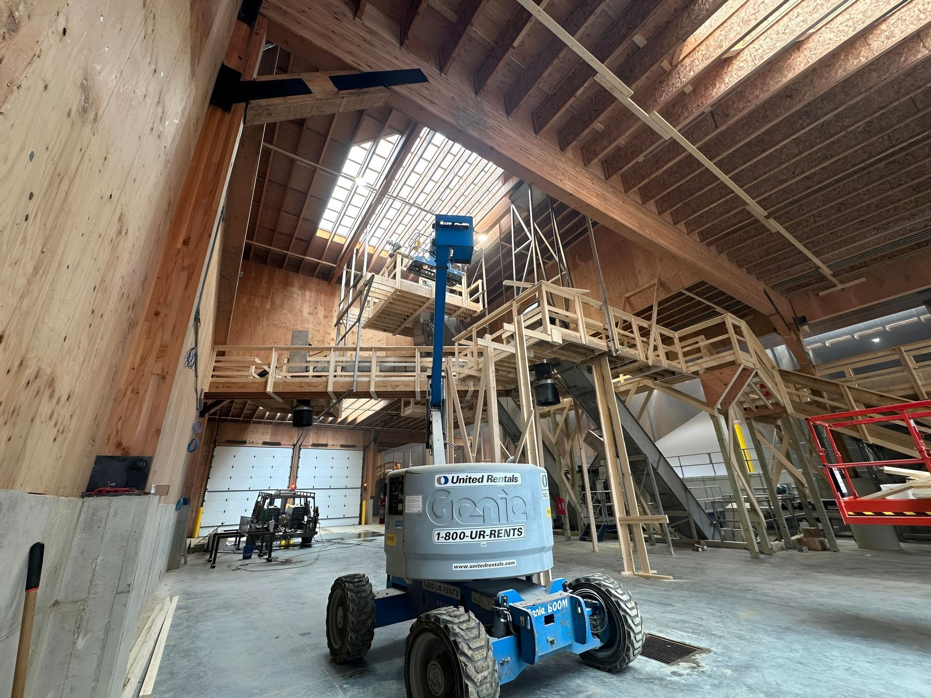 Construction site interior with a blue boom lift under a high wooden roof framework.