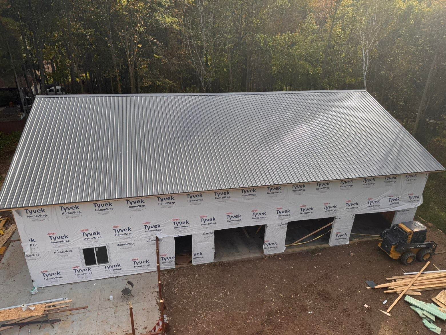 Partially built white house with a gray metal roof, seen from above in a wooded area