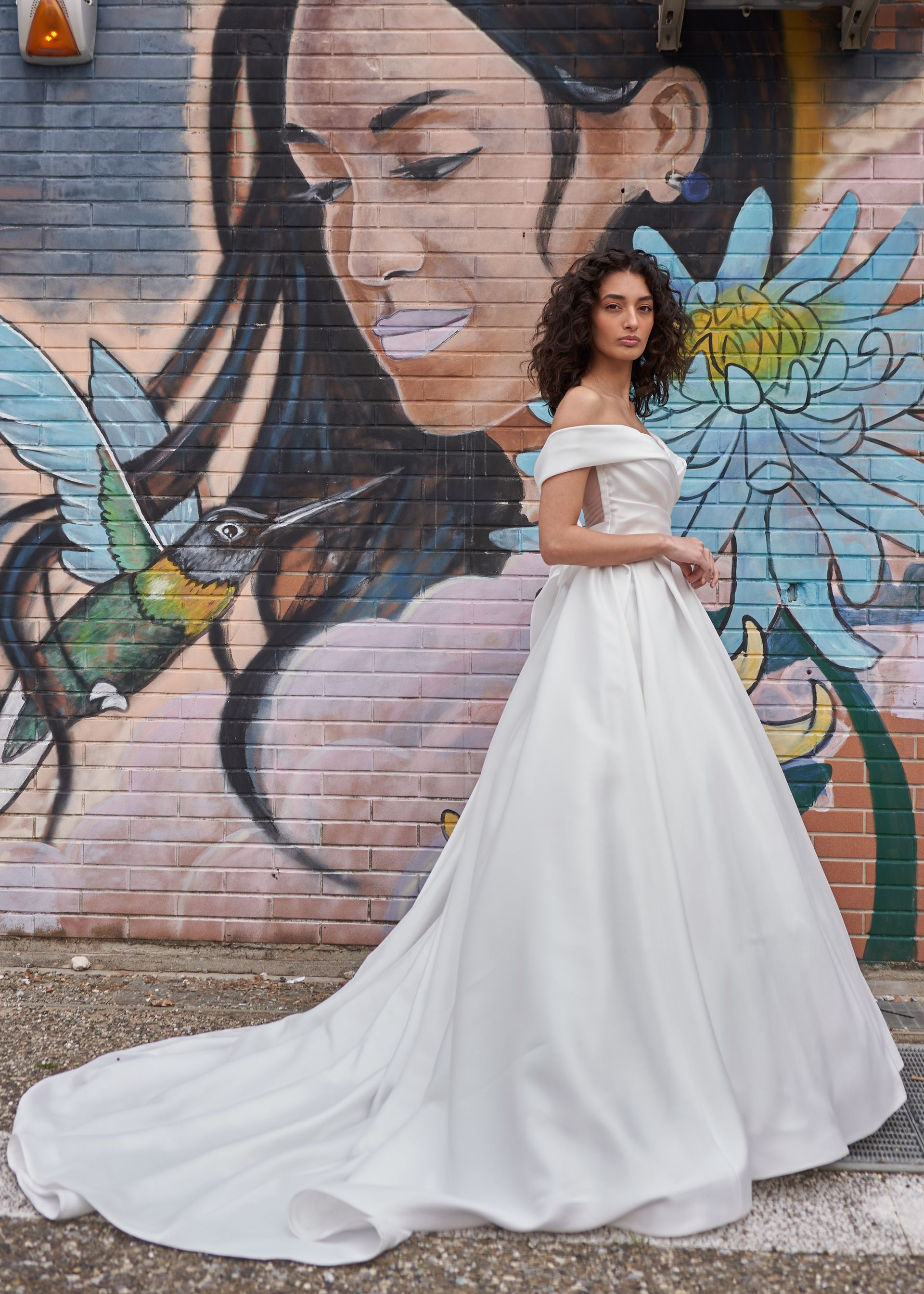 Una donna in abito da sposa è in piedi davanti a un murale su un muro.