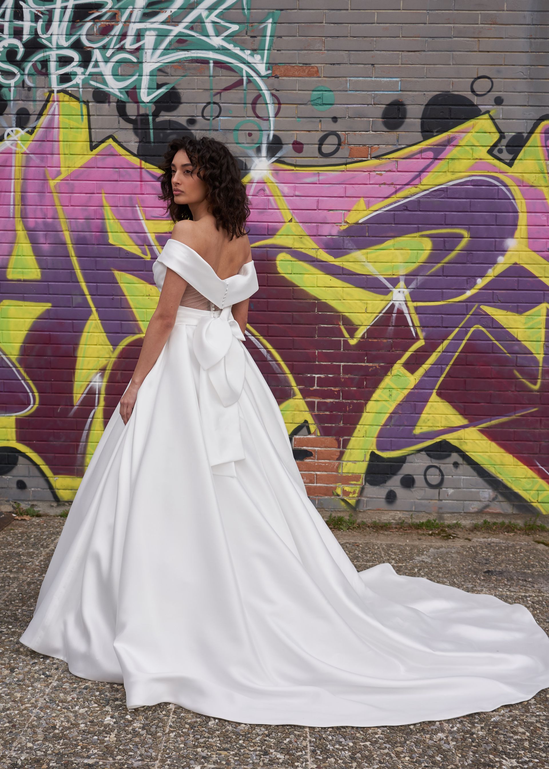 Una donna con un abito da sposa bianco è in piedi davanti a un muro di graffiti.
