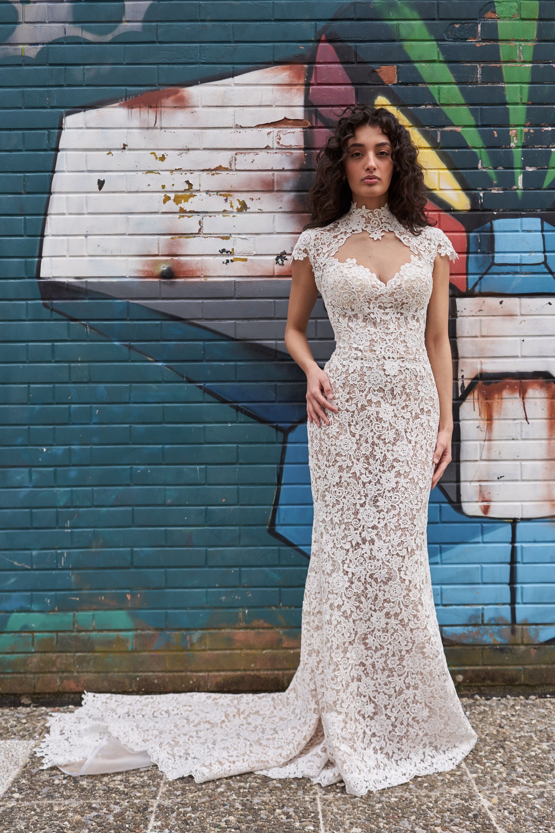 Una donna in abito da sposa è in piedi davanti a un muro di mattoni decorato con graffiti.