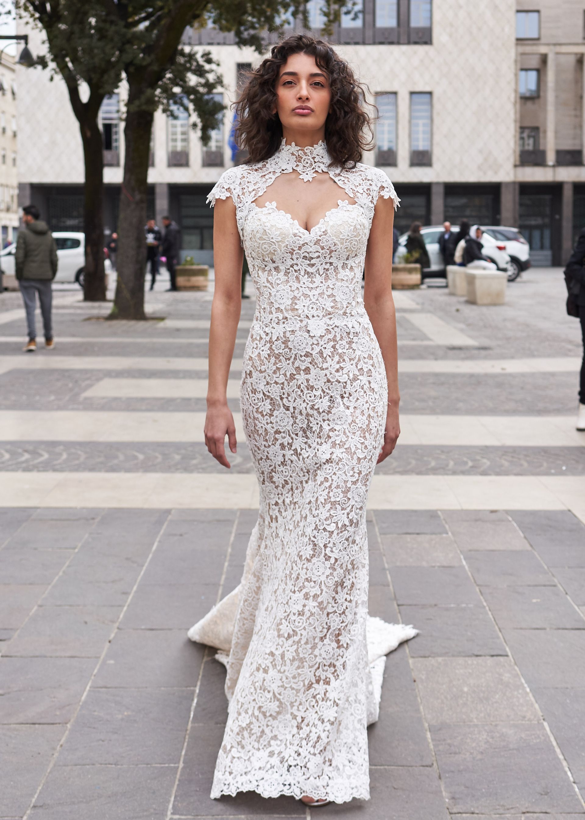 Una donna con un vestito di pizzo bianco è in piedi sul marciapiede.