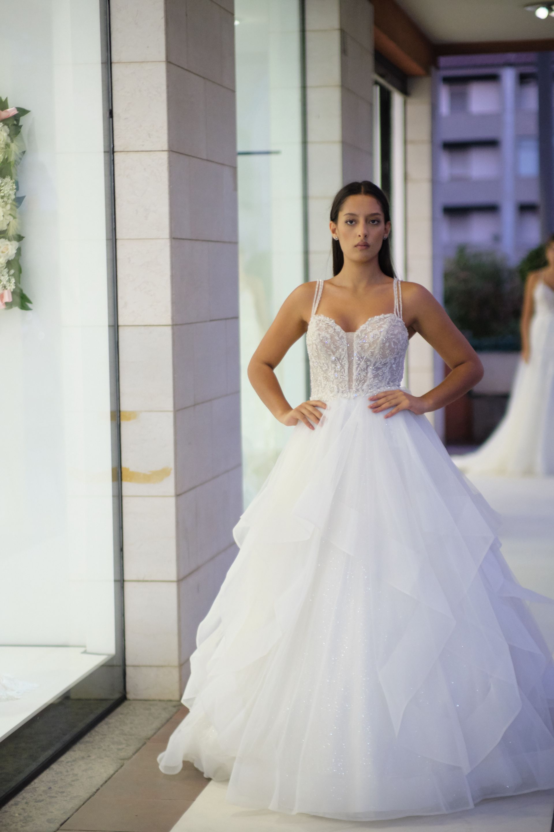 Una donna in abito da sposa bianco è in piedi davanti a una finestra.