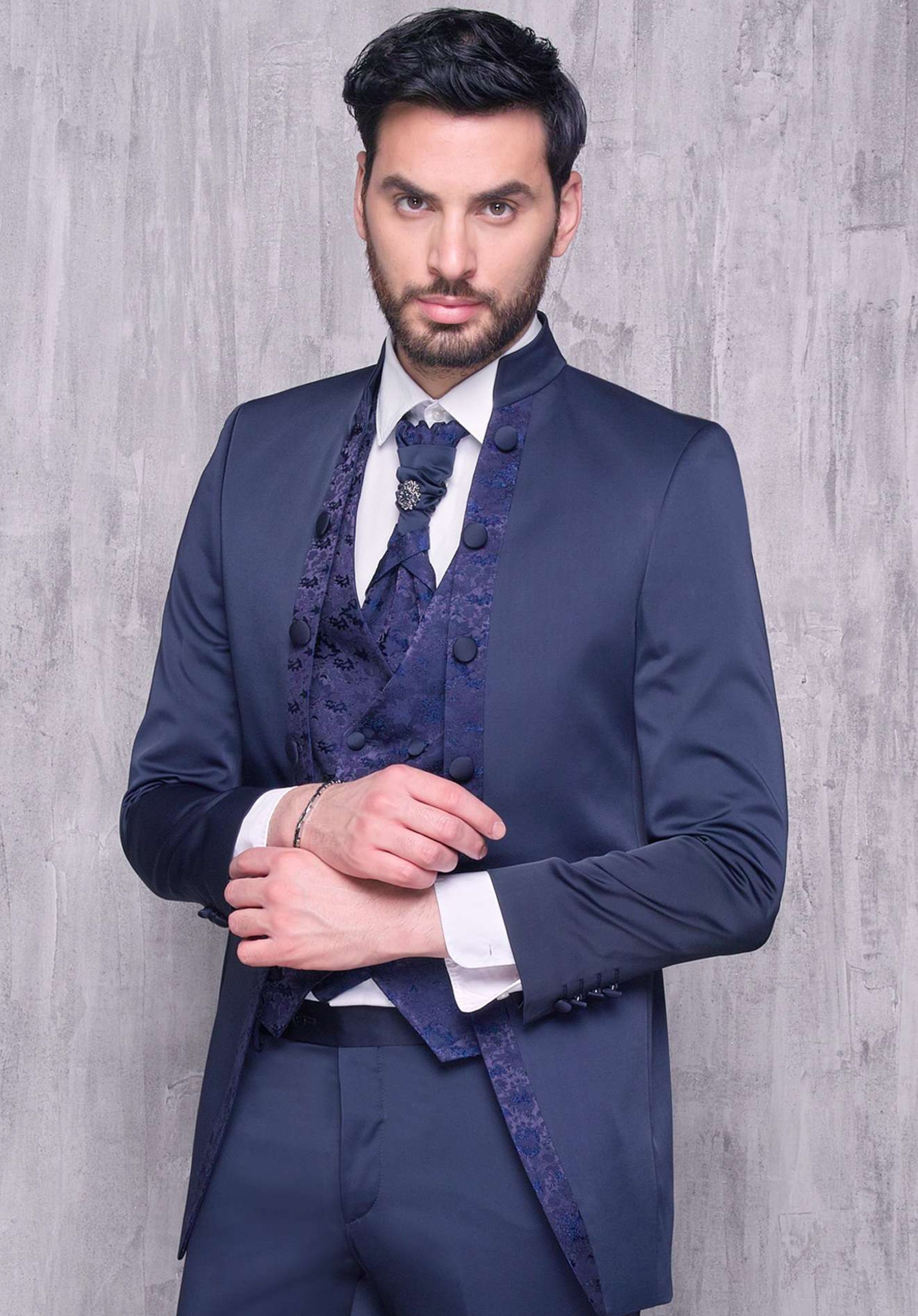 Un uomo in abito blu e cravatta è in piedi davanti a un muro.