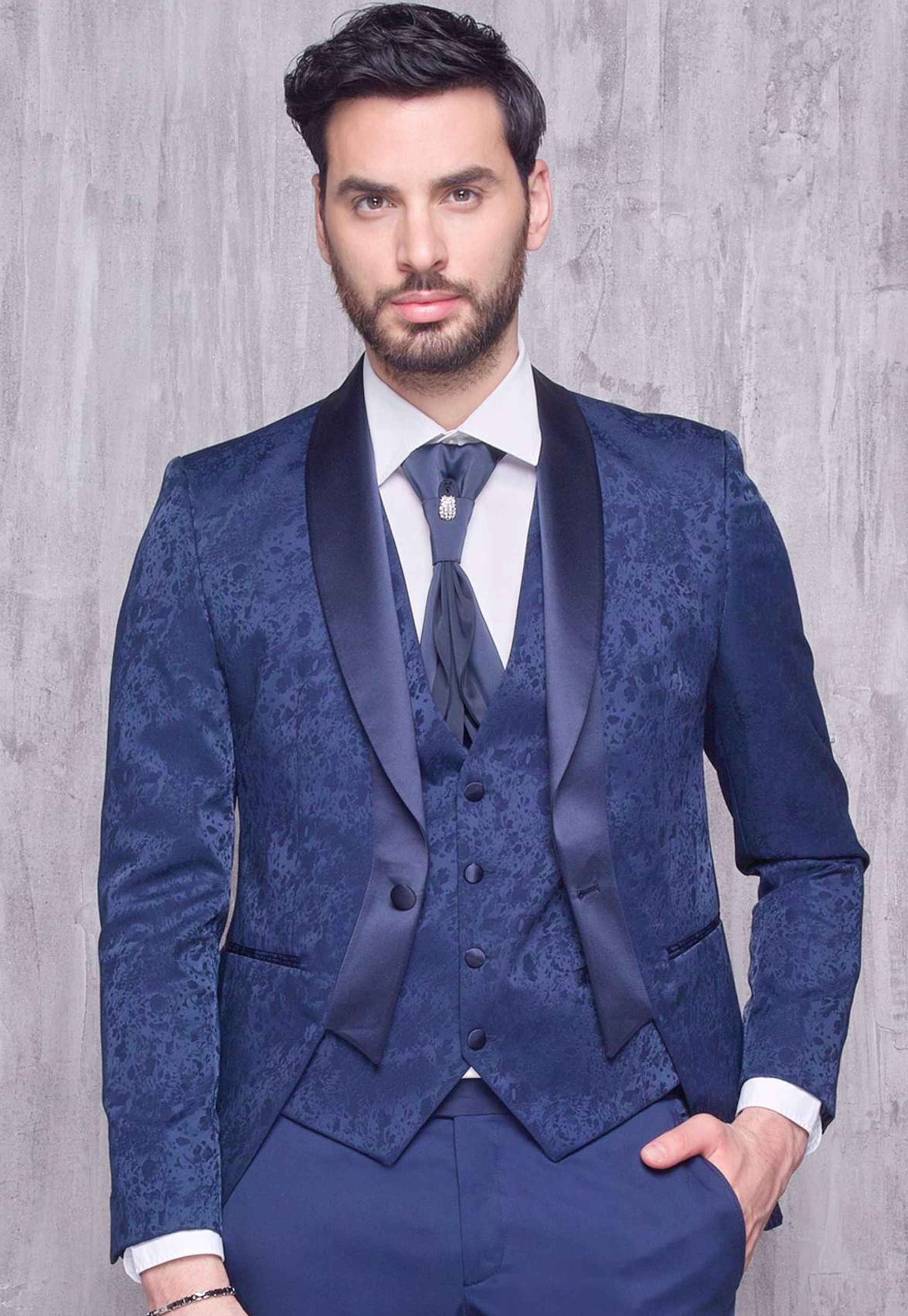 Un uomo in abito blu e cravatta è in piedi con le mani in tasca.