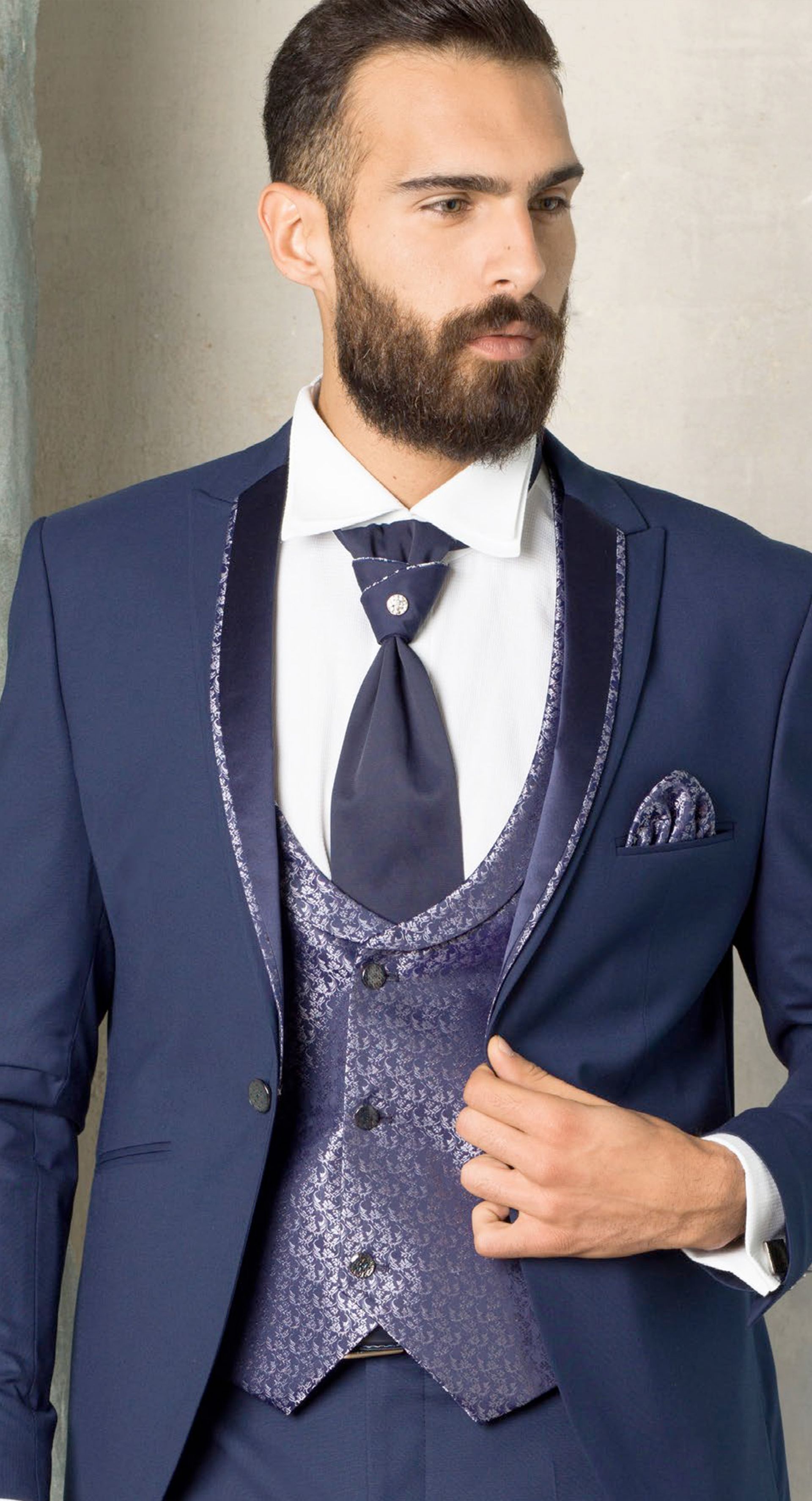 Un uomo con la barba indossa un abito blu e una cravatta.