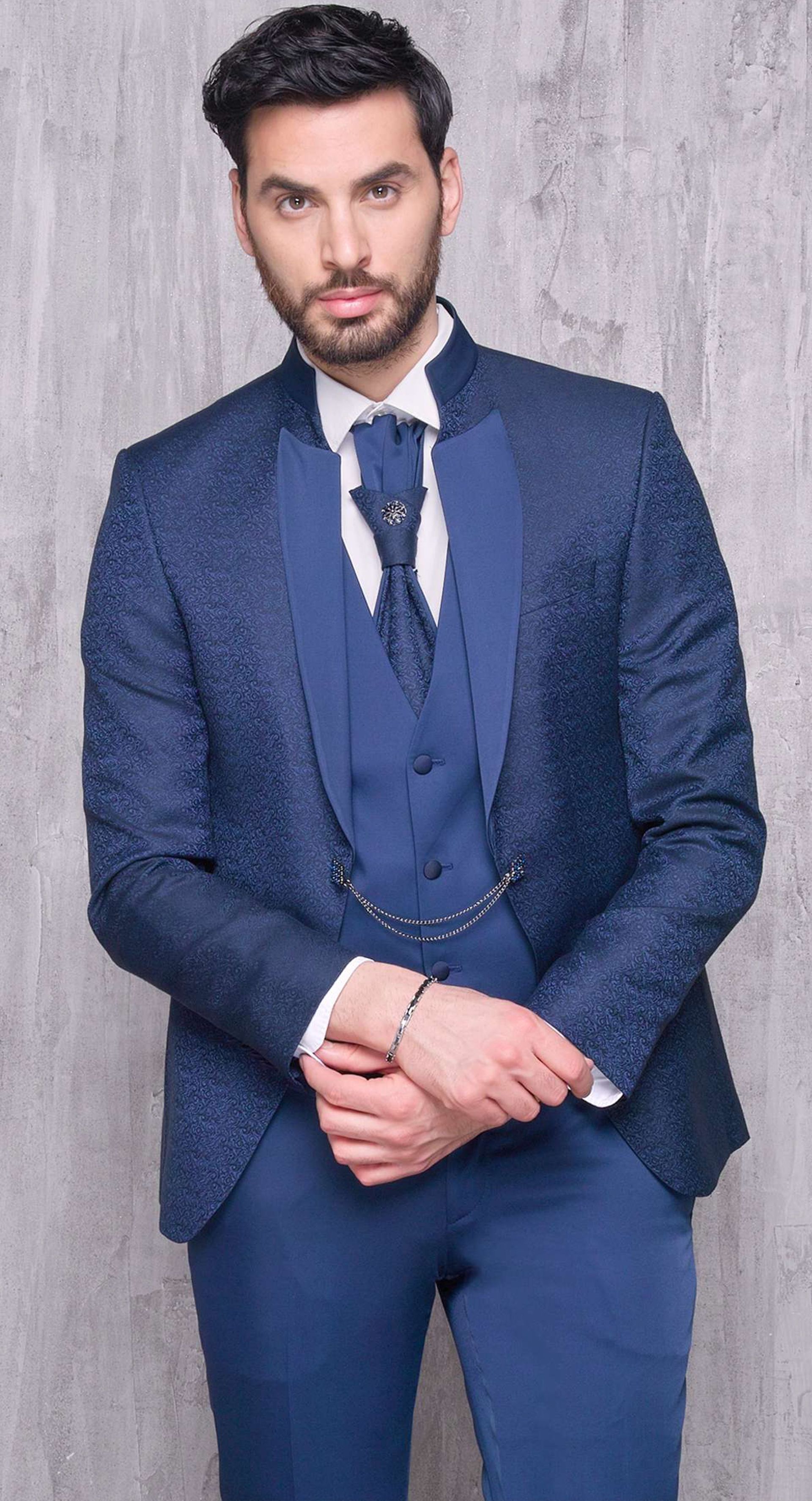 Un uomo in abito blu e cravatta è in piedi davanti a un muro.