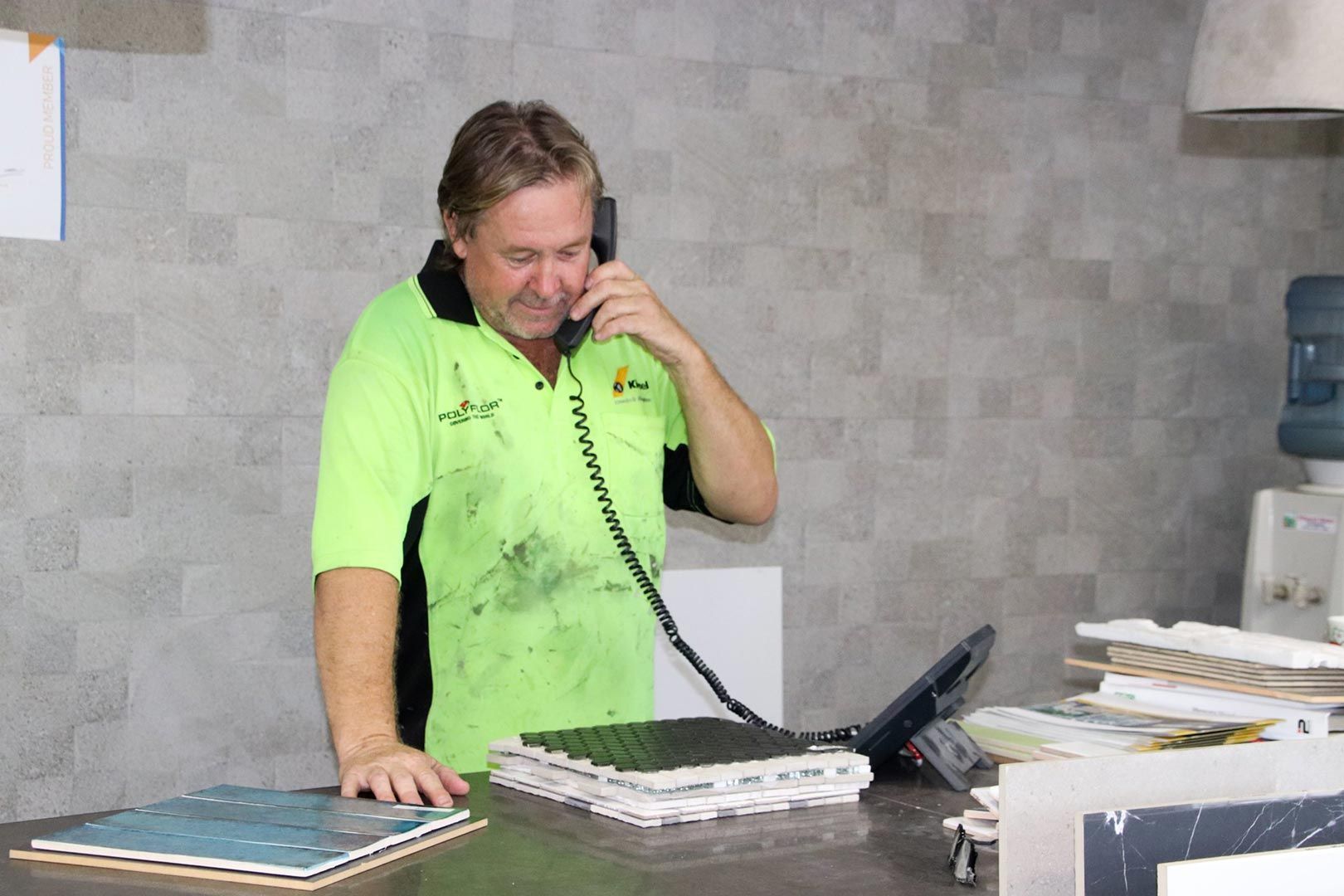 A Man in A Neon Green Shirt Is Talking on A Phone — Traditional Tiles & Flooring In Woree, QLD