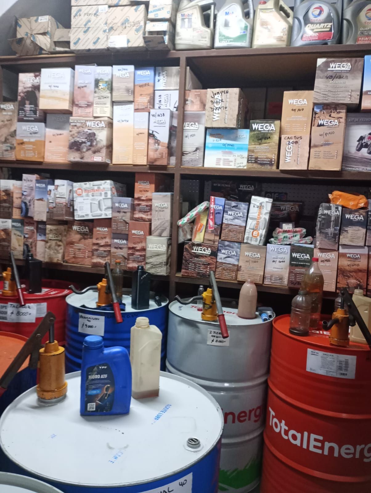 Filas de productos embalados en estantes sobre barriles industriales rojos en un almacén.