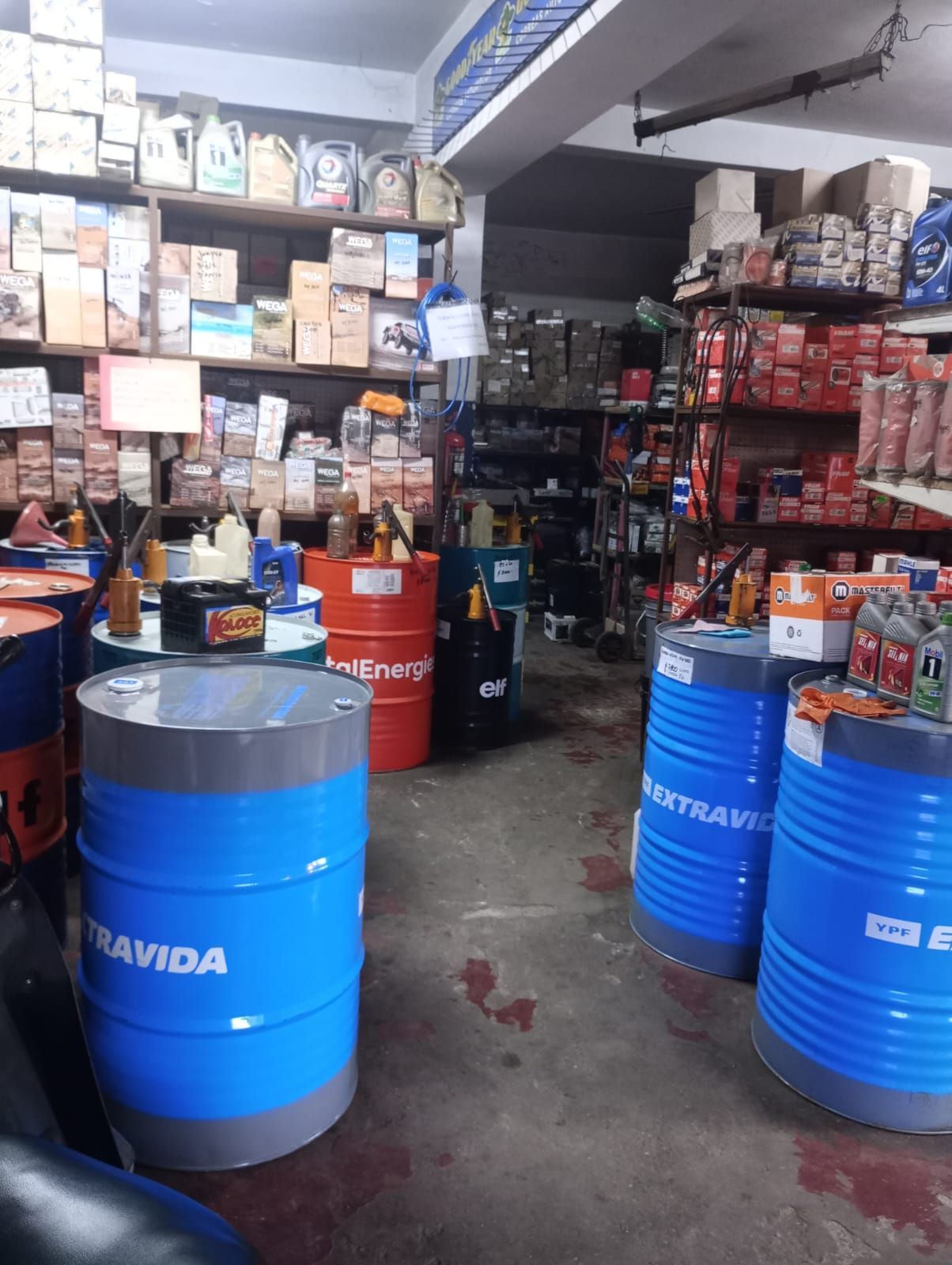 Tienda de repuestos para automóviles con bidones de aceite azules y estantes llenos de cajas de productos.