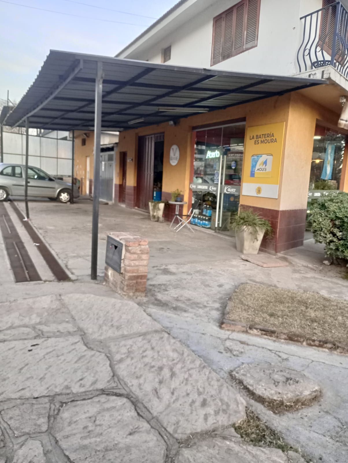Escaparate cubierto con rampa, acera agrietada y coche aparcado junto a un edificio amarillo.