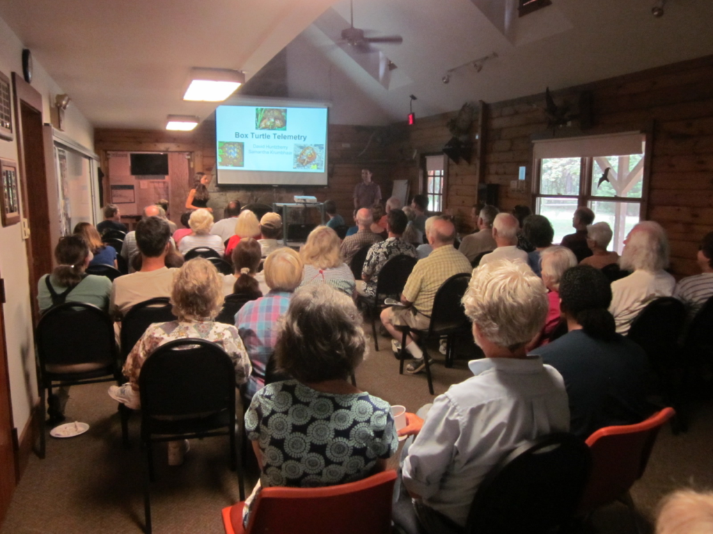 Audience seated in a hall watching a presentation on a projector screen